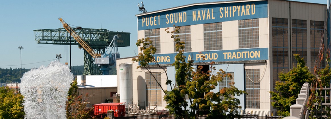 Building 460 can be seen in the foreground with the historical hammerhead crane in the background at Puget Sound Naval Shipyard & Intermediate Maintenance Facility, as seen from the waterfront park near the Washington State Ferries terminal in Bremerton, Washington.